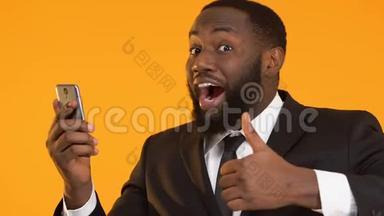 快乐的黑人穿着西装拿着智能手机，竖起大拇指，用现金回馈应用程序